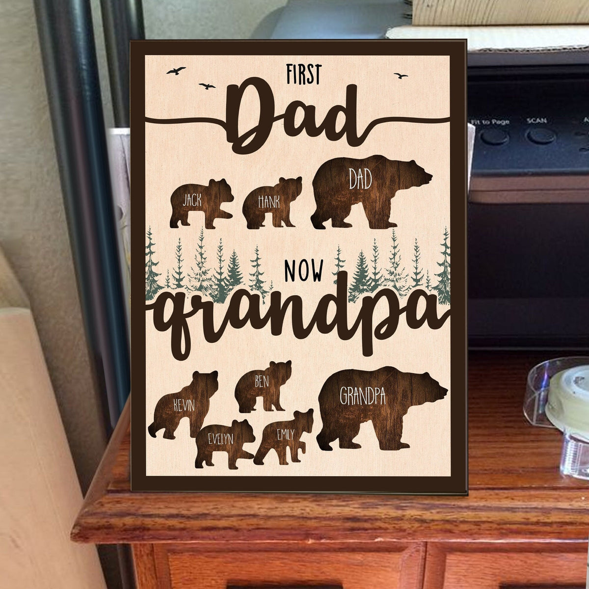 May include: A brown wooden sign with the text "First Dad Now Grandpa" in brown lettering. The sign features a silhouette of a bear family with the names "Jack", "Hank", "Dad", "Ben", "Kevin", "Evelyn", "Emily", and "Grandpa" written on each bear.