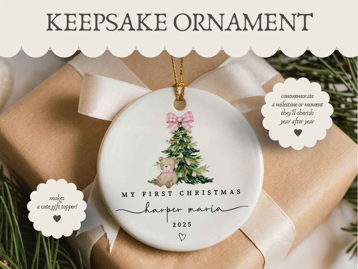May include: A round white ceramic ornament featuring a watercolor illustration of a green Christmas tree with a pink gingham bow and a teddy bear. The text reads MY FIRST CHRISTMAS, Harper Maria, and 2025, with a small heart icon below.