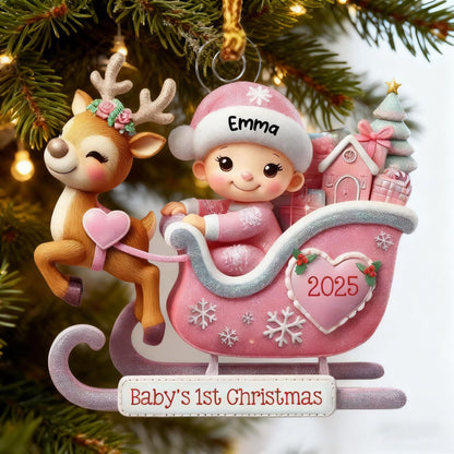 May include: A Christmas ornament featuring a reindeer with a floral wreath and a baby in a pink hat sitting in a pink sleigh. The sleigh displays a heart with the year 2025, a small house, and a tree. The base reads Baby's 1st Christmas and Emma.