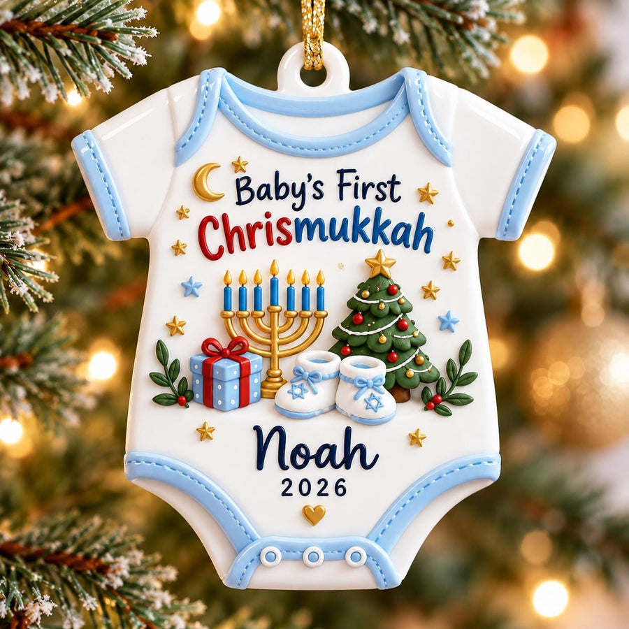 May include: A white baby bodysuit-shaped Christmas ornament with light blue trim. It features the text "Baby's First Chrismukkah", a gold menorah, a decorated Christmas tree, a blue gift box, and baby booties. The name "Noah" and "2026" are printed.