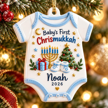May include: A white ceramic ornament shaped like a baby onesie with light blue trim. It features the text Baby's First Chrismukkah, a gold menorah, a decorated Christmas tree, a blue gift box, baby booties, the name Noah, and the year 2026.