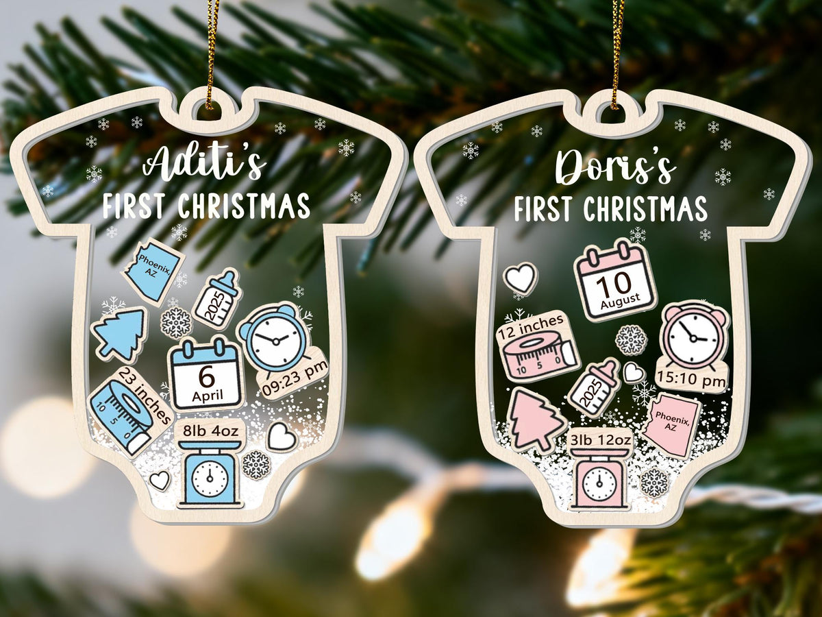 May include: Two baby onesie-shaped Christmas ornaments. One is blue and the other is pink. Each ornament has a name and "FIRST CHRISTMAS" printed on it. The blue ornament has the name "Aditi" and the pink ornament has the name "Doris". Each ornament has birth details.