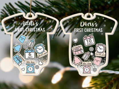 May include: Two baby onesie-shaped Christmas ornaments. One is blue and the other is pink. Each ornament has a name and "FIRST CHRISTMAS" printed on it. The blue ornament has the name "Aditi" and the pink ornament has the name "Doris". Each ornament has birth details.