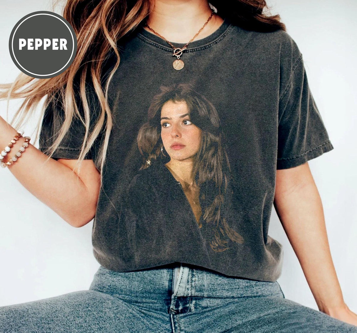 Dark gray t-shirt featuring a portrait of a woman with long brown hair. The image is printed on the front of the shirt. The word "PEPPER" is in a circle in the upper left corner of the image.