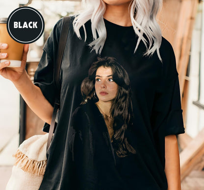 Black oversized t-shirt featuring a portrait of a woman with long dark hair. The word "BLACK" is printed in a white font inside a black circle on the upper left. The shirt has rolled-up sleeves.