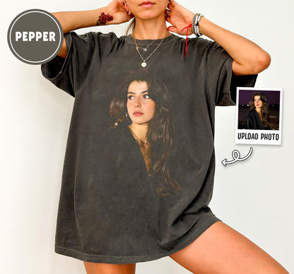 Dark gray oversized t-shirt featuring a portrait of a woman. The shirt has a vintage, distressed look. A small photo with the text "UPLOAD PHOTO" is on the right side. The word "PEPPER" is in a circle on the left.