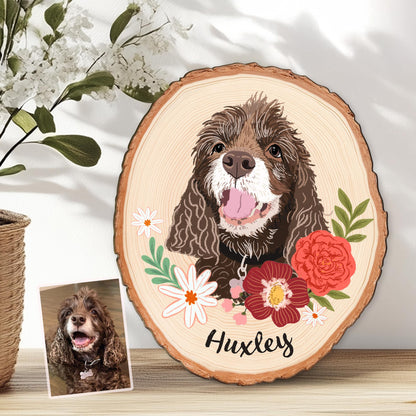 May include: A wood slice featuring a brown dog portrait with a floral wreath of red and white flowers and green leaves. The dog's name, "Huxley," is written in black script. A smaller photo of the dog is also present.