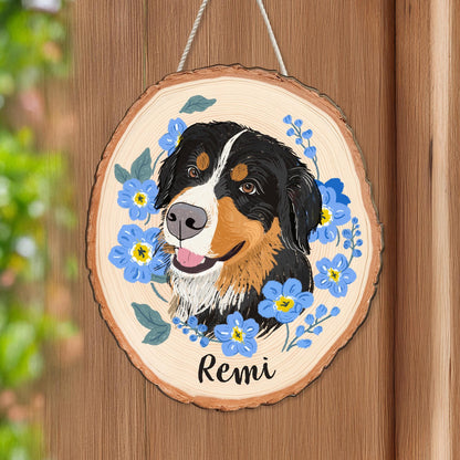 May include: A round wooden sign featuring a painted Bernese Mountain Dog portrait surrounded by blue flowers. The dog has black, brown, and white fur, with the name "Remi" written below in cursive.