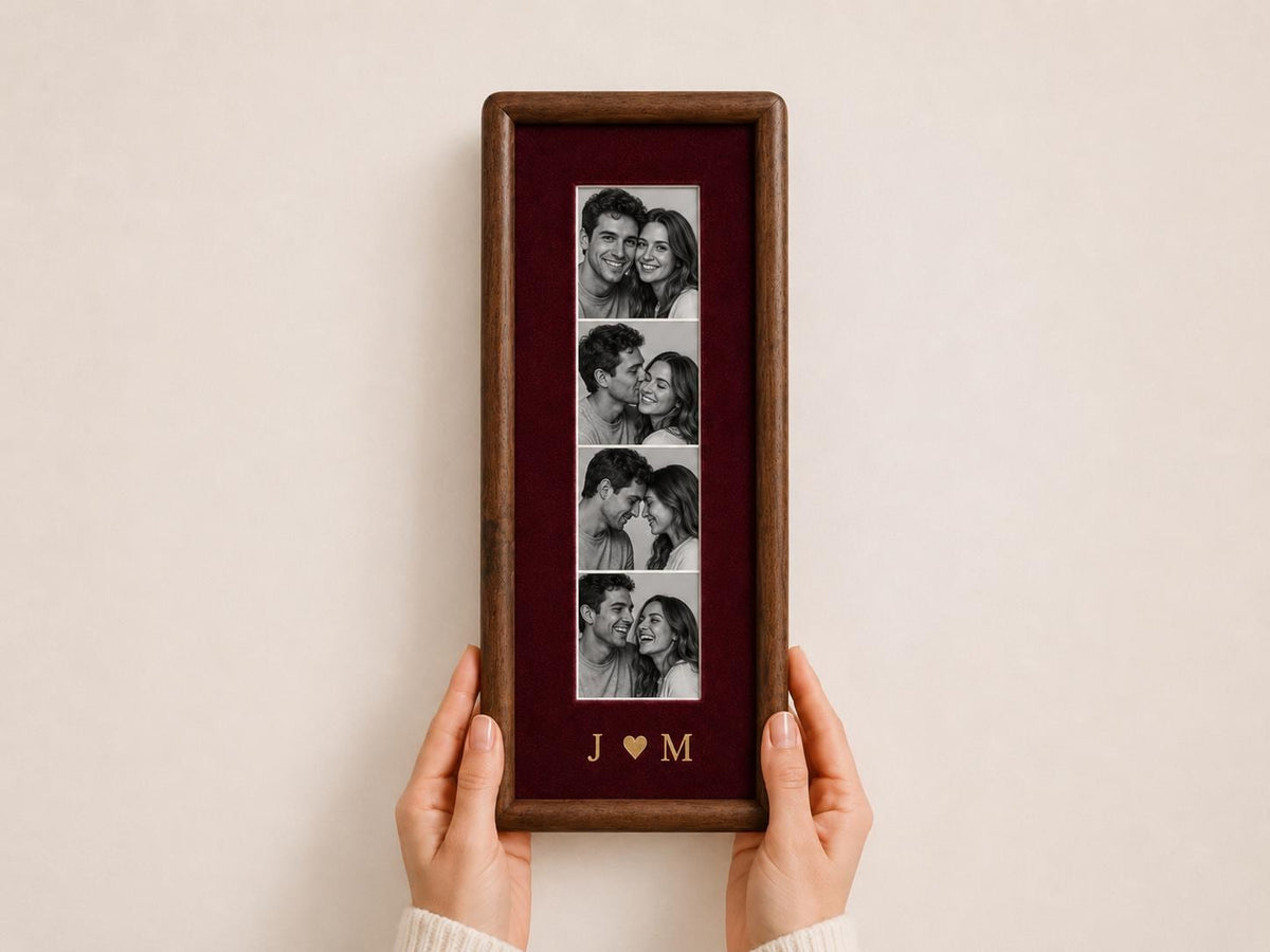 A rectangular dark wood picture frame featuring a deep burgundy velvet mat. The frame displays a vertical strip of four black and white photographs of a couple. Below the photos, the gold letters J and M are separated by a heart.