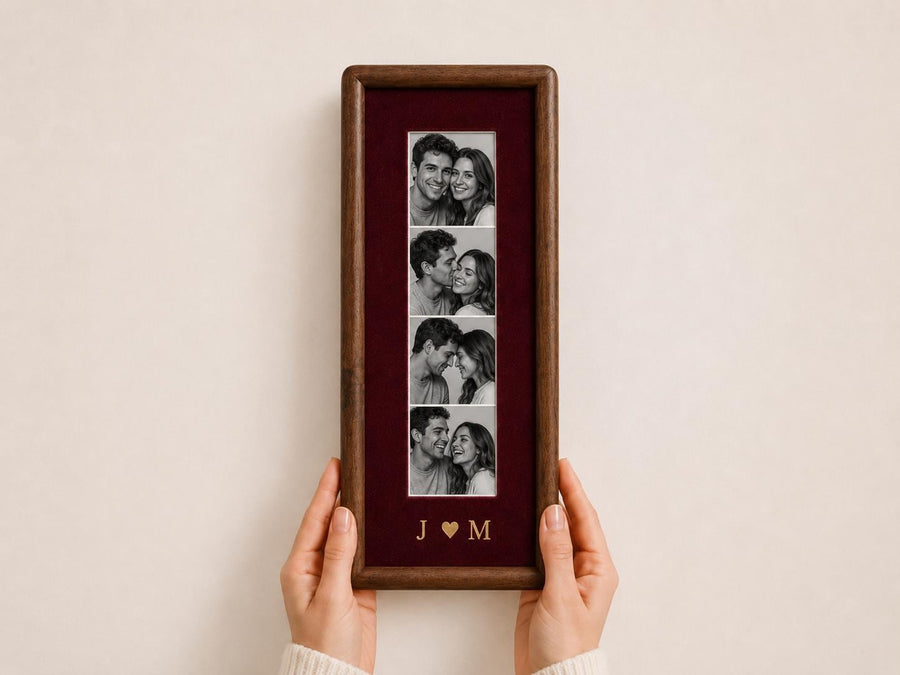 A rectangular dark wood picture frame featuring a deep burgundy velvet mat. The frame displays a vertical strip of four black and white photographs of a couple. Below the photos, the gold letters J and M are separated by a heart.