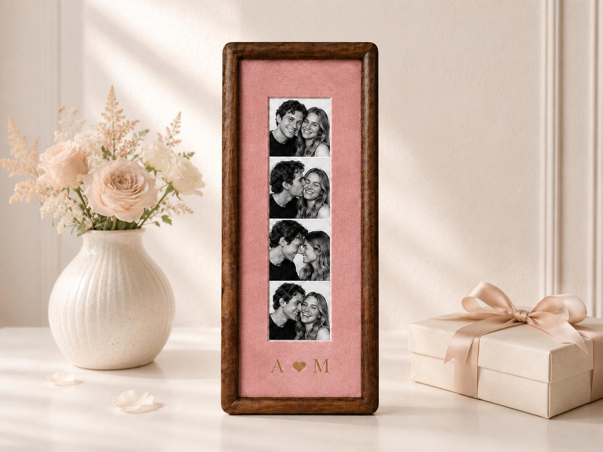 A tall, rectangular wooden picture frame with a dark brown finish, featuring a vertical strip of four black and white photographs of a couple. The photos are set against a dusty pink mat with the gold-colored letters A and M separated by a heart.