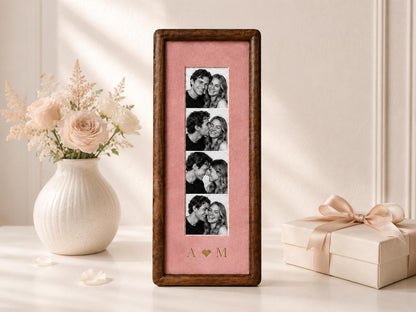 A tall, rectangular wooden picture frame with a dark brown finish, featuring a vertical strip of four black and white photographs of a couple. The photos are set against a dusty pink mat with the gold-colored letters A and M separated by a heart.