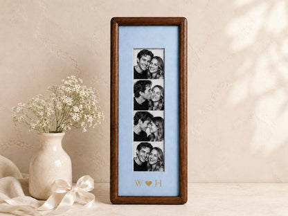 A vertical rectangular dark wood picture frame containing a light blue mat board with four stacked black and white photographs of a couple. The mat board features the gold-colored letters W and H separated by a heart symbol.
