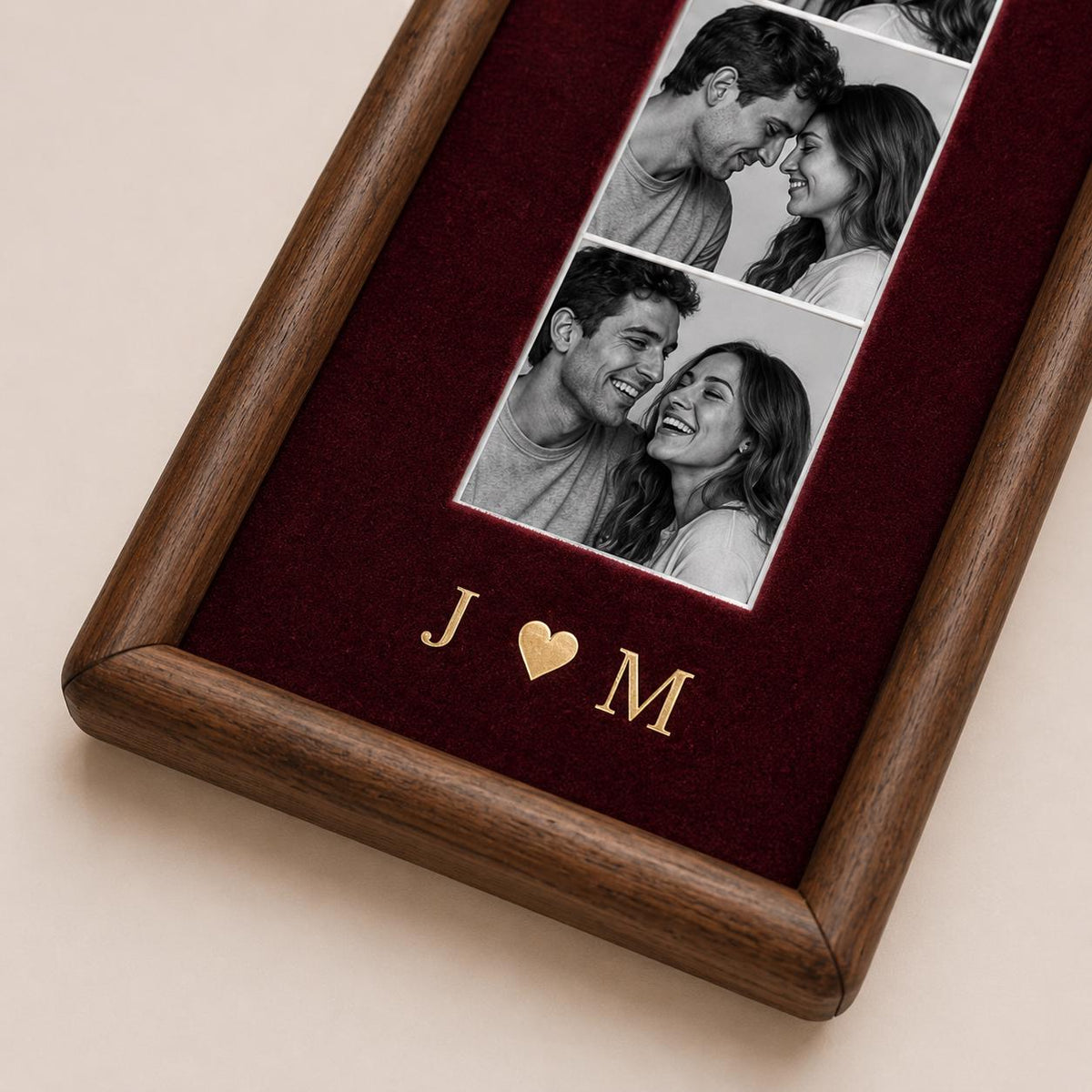 A rectangular wooden picture frame featuring a deep burgundy velvet backing. The frame displays two black and white photographs of a couple. Below the photos, the gold-colored letters J and M are separated by a gold heart symbol.