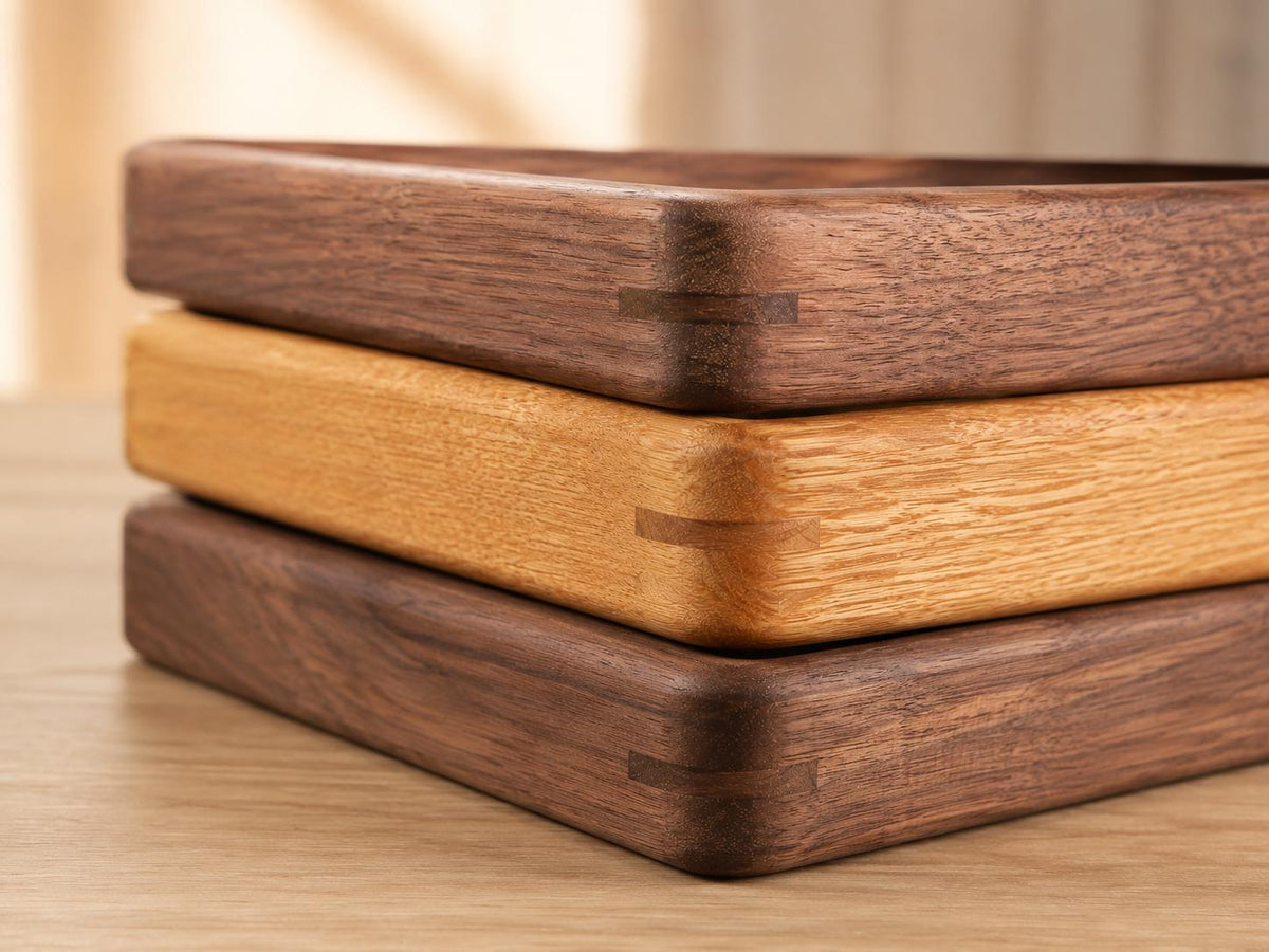 A stack of three rectangular wooden trays with rounded corners. The top and bottom trays are made of dark brown walnut wood, while the middle tray is made of light tan oak wood. Each tray features visible spline joinery details.