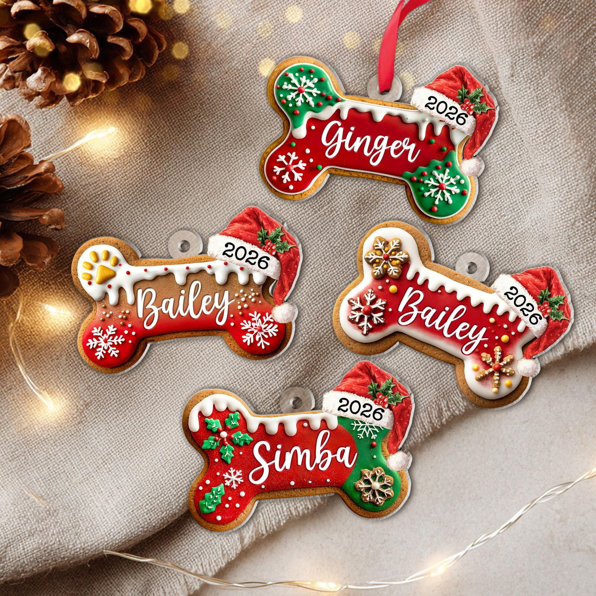 May include: Four bone-shaped Christmas ornaments featuring white icing, red and green accents, and snowflake patterns. Each ornament displays a name in white script—Ginger, Bailey, or Simba—and the year 2026 printed on a red Santa hat.