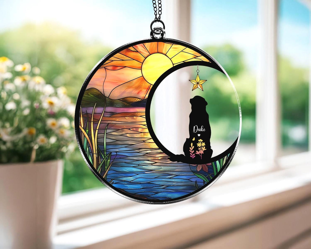 May include: A round stained glass suncatcher featuring a dog silhouette inside a crescent moon. The background depicts a sunset over a lake. The dog's name, "Duke", is written on the moon. A star hangs from the moon.