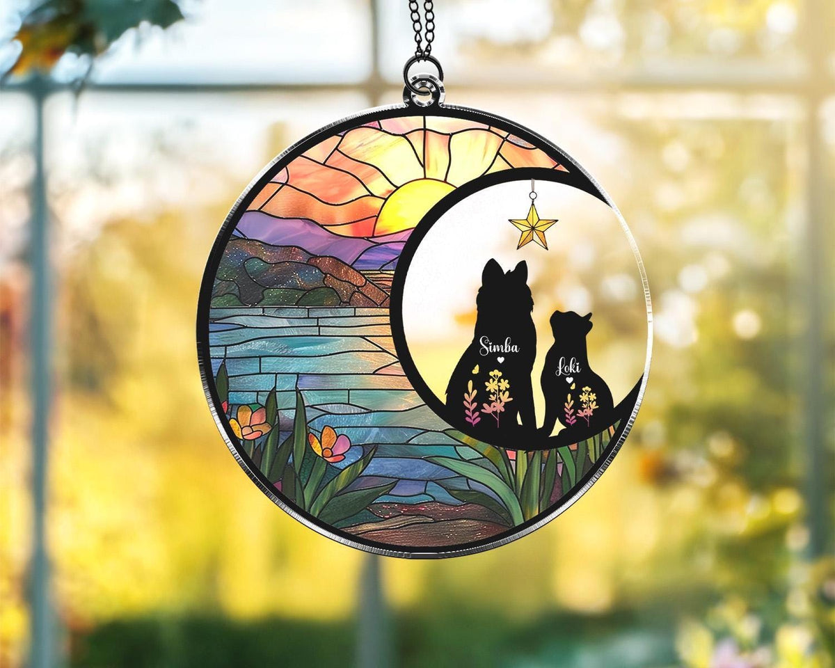 May include: A round stained glass suncatcher featuring a crescent moon with two dog silhouettes, Simba and Loki, and a hanging star. The background depicts a sunset over a lake with mountains and flowers.