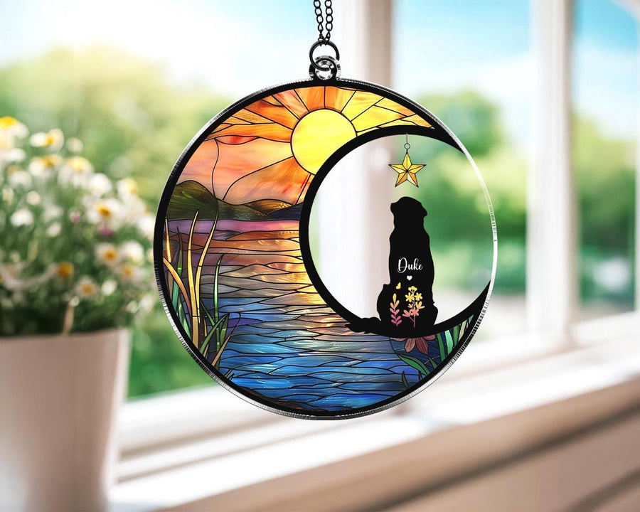 May include: A round stained glass suncatcher featuring a dog silhouette inside a crescent moon. The background depicts a sunset over a lake. The dog's name, "Duke", is written on the moon. A star hangs from the moon.