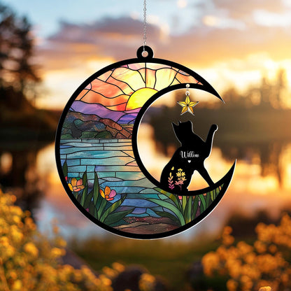May include: A stained glass-style suncatcher featuring a black cat silhouette seated on a crescent moon. The moon frames a colorful sunset scene with a lake and mountains. A gold star hangs above the cat, and the name "Willow" is inscribed on the cat.