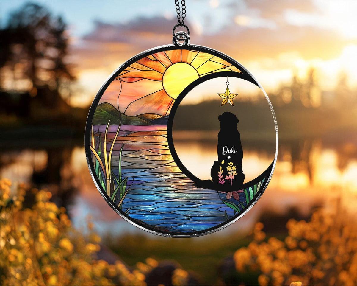 May include: Round stained glass suncatcher featuring a dog silhouette inside a crescent moon. The scene includes a sunset over a lake with colorful reeds. A gold star hangs from the moon. The dog's name, "Duke", is written on the moon.