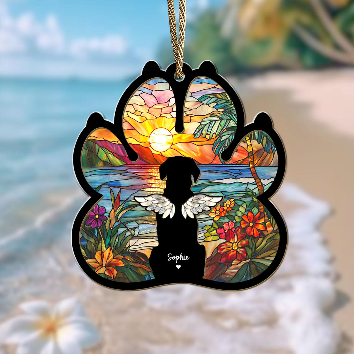 May include: A stained glass paw print ornament with a silhouette of a dog with wings in front of a sunset over a tropical beach. The ornament is personalized with the name "Sophie".