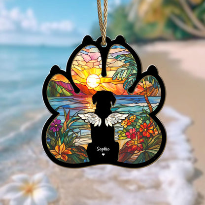 May include: A stained glass paw print ornament with a silhouette of a dog with wings in front of a sunset over a tropical beach. The ornament is personalized with the name "Sophie".
