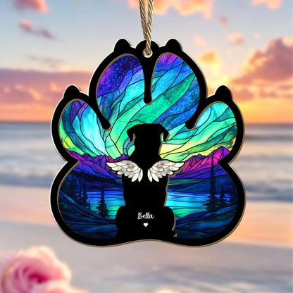 May include: A stained glass paw print ornament with a silhouette of a dog with wings and the name "Bella" in the center. The background is a colorful aurora borealis scene.