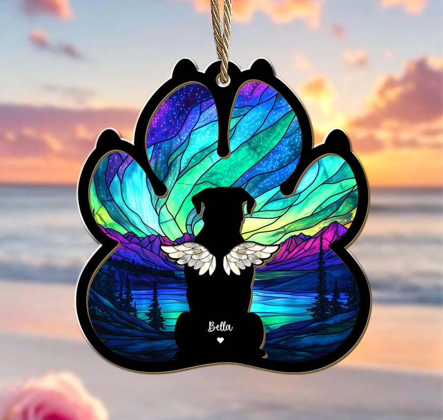 May include: A stained glass paw print ornament with a silhouette of a dog with wings and the name "Bella" in the center. The background is a colorful aurora borealis scene with mountains and a lake.