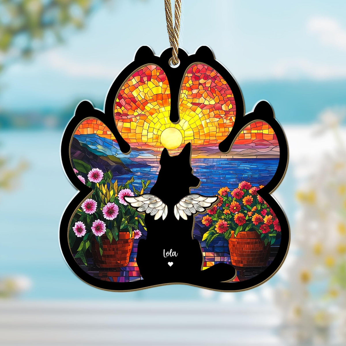 May include: A stained glass paw print ornament with a sunset scene and a black silhouette of a dog with wings. The dog's name, "Lola", is written below the silhouette.