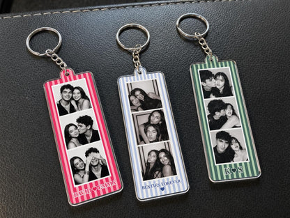 Three rectangular acrylic keychains with metal rings, each featuring vertical stripes in pink, light blue, or green. Each keychain displays three black and white photo strips of couples. Text includes DAVID HEART EMMA, BESTIES FOREVER with a heart, and K HEART S.