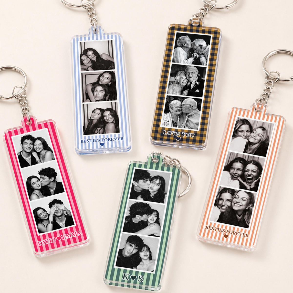 Five rectangular acrylic keychains with metal rings, each featuring a vertical strip of three black and white photos and a colored striped border. Text includes "BESTIES FOREVER," "LOVE YOU," "DAVID EMMA," and "K S" with small heart icons.