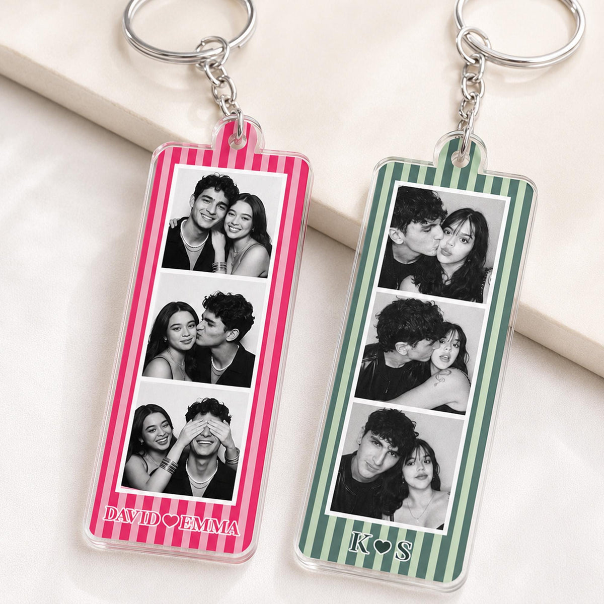 Two rectangular acrylic keychains with silver metal rings and chains. The left keychain has pink vertical stripes and the text DAVID EMMA. The right keychain has green vertical stripes and the text K S. Both feature three black and white photos.