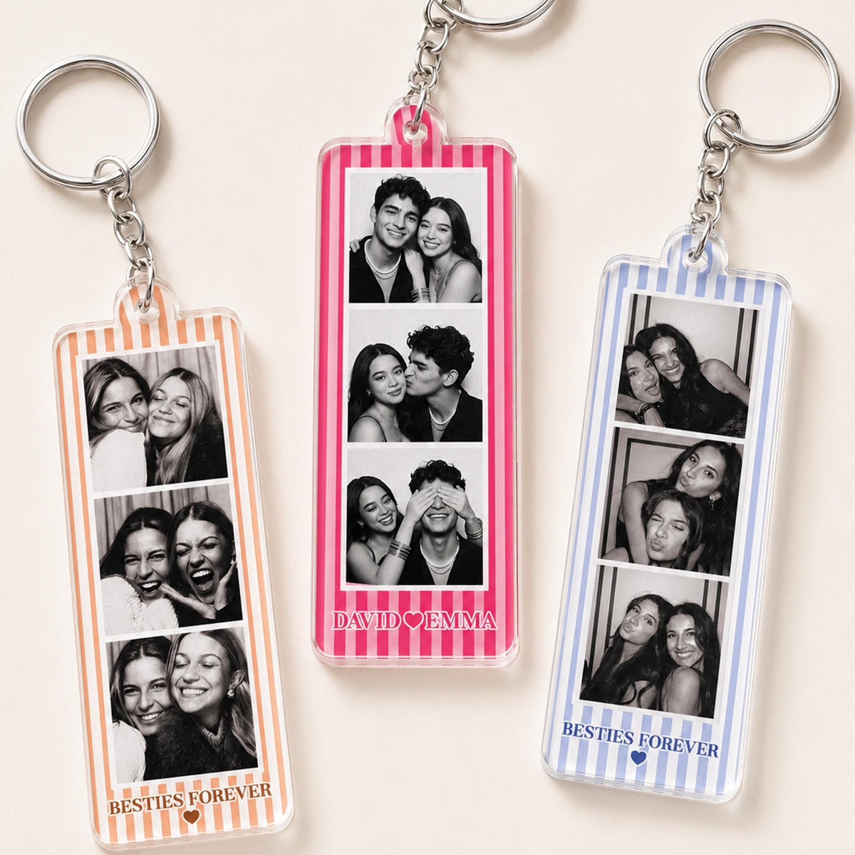Three rectangular acrylic keychains with metal rings. Each features a vertical strip of three black and white photo booth images. The left keychain has orange stripes and says BESTIES FOREVER. The center has pink stripes and says DAVID HEART EMMA. The right has blue stripes and says BESTIES FOREVER.
