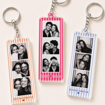 Three rectangular acrylic keychains with metal rings. Each features a vertical strip of three black and white photo booth images. The left keychain has orange stripes and says BESTIES FOREVER. The center has pink stripes and says DAVID HEART EMMA. The right has blue stripes and says BESTIES FOREVER.