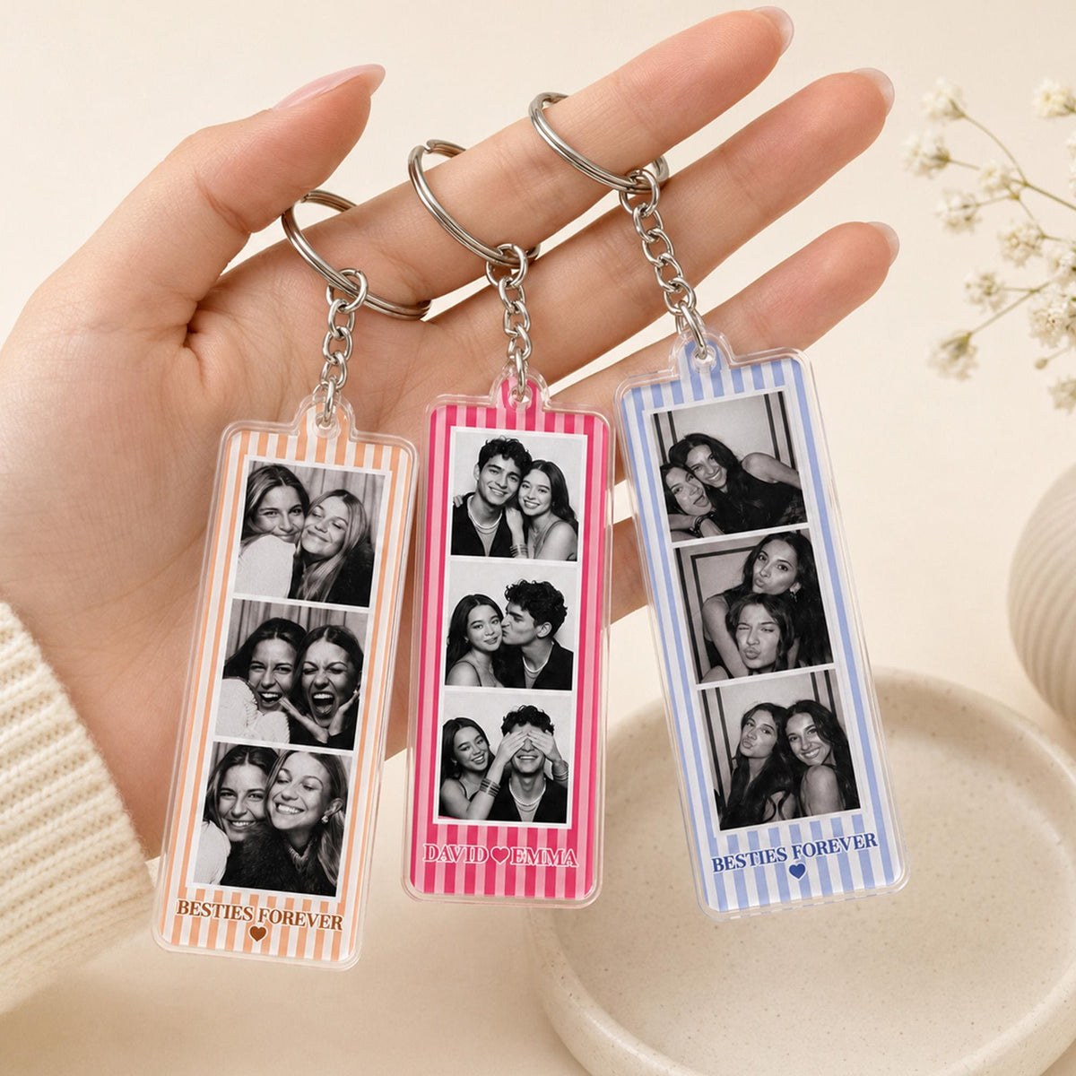 Three rectangular acrylic keychains with metal rings and chains. Each features vertical stripes in orange, pink, or blue, and three black and white photo strips. The keychains display the text BESTIES FOREVER or DAVID HEART EMMA.