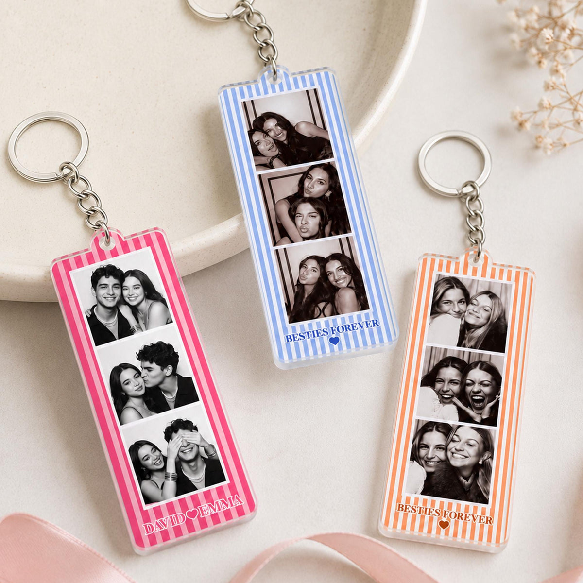 Three rectangular acrylic keychains with metal rings, each featuring a vertical striped border in pink, blue, or orange. Each keychain displays three black and white photo strips and text at the bottom reading "BESTIES FOREVER" or "DAVID EMMA".