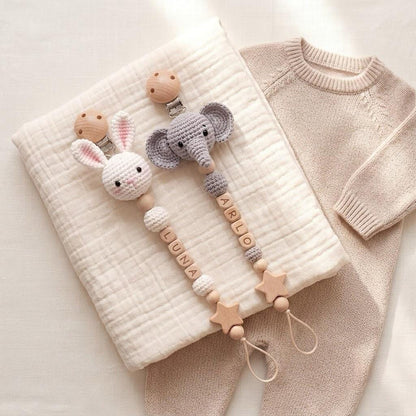 Two pacifier clips featuring crocheted animal heads, one a white rabbit and one a gray elephant. Each clip includes wooden beads, some engraved with the names LUNA and ARLO, and wooden star-shaped accents with a loop at the bottom.
