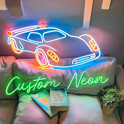 A neon sign with a green outline that says "Custom Neon" and a colorful neon car design. The sign is on a gray couch with a book titled "Inheritance" by Christopher Paolini.