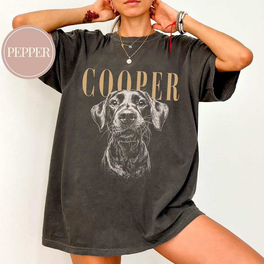 Dark gray t-shirt featuring a detailed illustration of a dog's face, with the name "COOPER" printed above in a tan color. The shirt has a vintage, worn look.