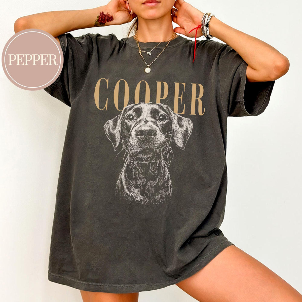 Dark gray t-shirt featuring a detailed illustration of a dog's face, with the name "COOPER" printed above in a tan color. The shirt has a vintage, worn look.