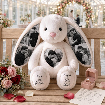 A cream-colored plush rabbit featuring black and white photo prints on its ears and a heart-shaped patch on its chest. The feet are embroidered with the text Love you forever and Arthur & Chloe 2026. A pink velvet ring box sits nearby.