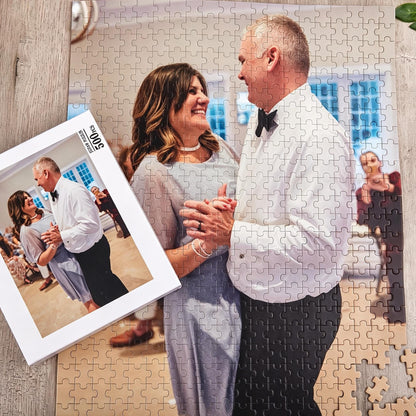 A 500-piece jigsaw puzzle featuring a photograph of a couple dancing. The person on the left wears a light blue dress, and the person on the right wears a white button-down shirt with a black bowtie and black trousers.