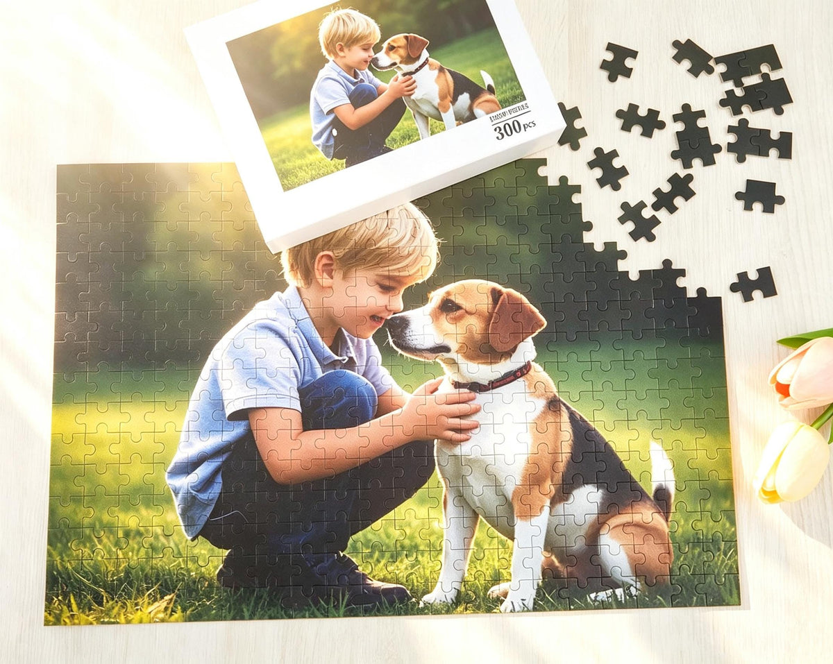 A 300-piece jigsaw puzzle featuring a photograph of a young child in a light blue shirt and dark pants kneeling in the grass with a beagle dog. The puzzle box shows the same image, and several loose black puzzle pieces are scattered nearby.