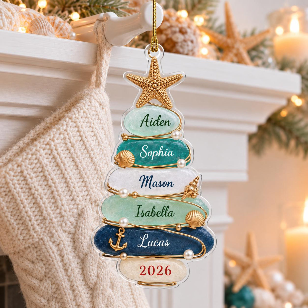 A Christmas tree-shaped ornament featuring six stacked, smooth, rounded stones in shades of light green, teal, white, and dark blue. The stones are inscribed with the names Aiden, Sophia, Mason, Isabella, Lucas, and the year 2026.