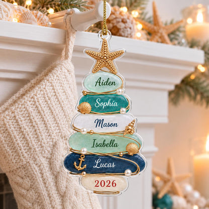 A Christmas tree-shaped ornament featuring six stacked, smooth, rounded stones in shades of light green, teal, white, and dark blue. The stones are inscribed with the names Aiden, Sophia, Mason, Isabella, Lucas, and the year 2026.