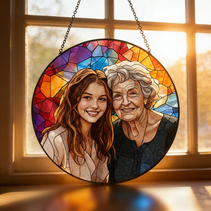 Round stained glass art piece featuring two smiling women. The background is a colorful mosaic of red, orange, yellow, blue, and purple. The piece is hanging from a chain in front of a window.