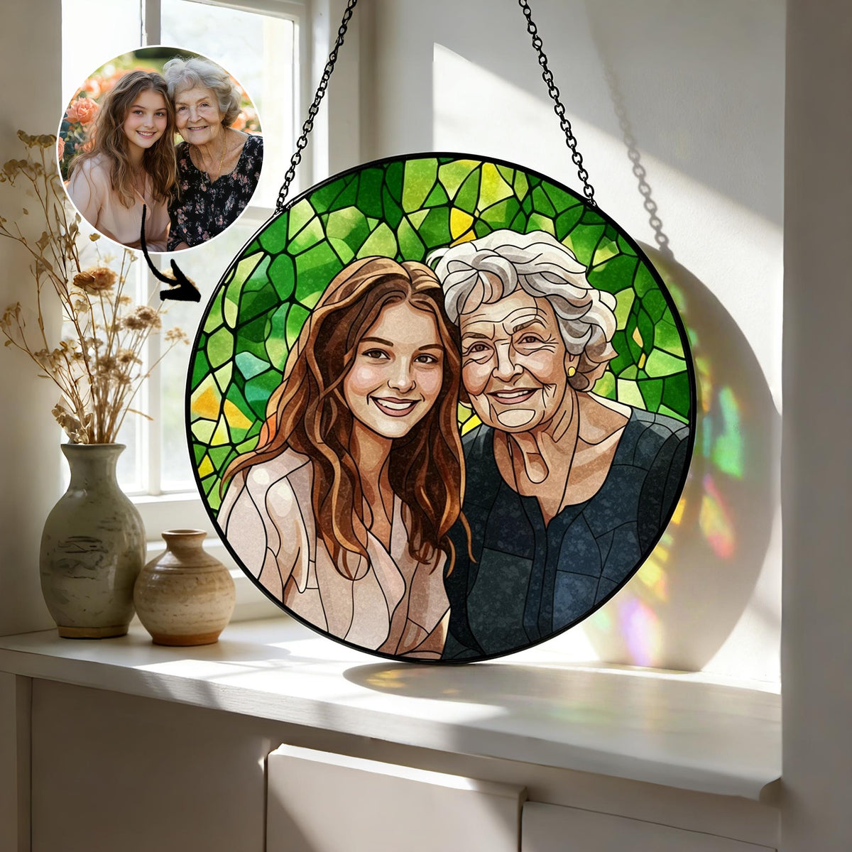 A round stained glass art piece featuring a portrait of two smiling women. The background is a mosaic of green glass. The artwork is suspended by a black chain. A smaller photo of the women is in the upper left corner.
