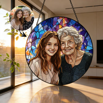 A round stained glass art piece featuring a portrait of two women. The artwork has a black border and is suspended by a chain. The background is a mosaic of blue, purple, and orange hues, with the women's faces in the center.