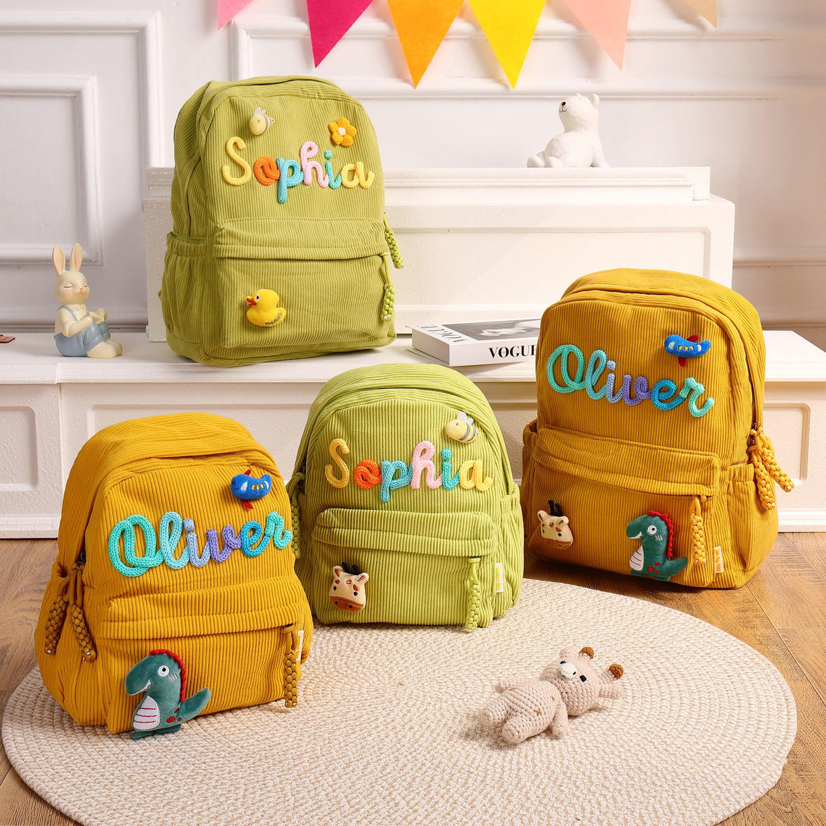 Four corduroy backpacks in olive green and mustard yellow. Each bag features a personalized name in colorful, raised, cursive lettering, along with small, plush, decorative patches including dinosaurs, bees, and ducks.